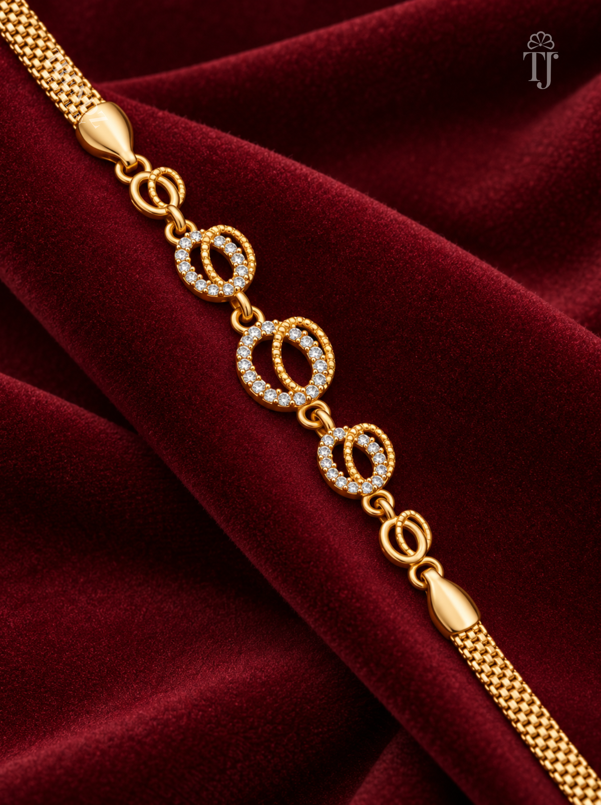 A gold chain bracelet with interlocking oval links, some set with clear stones, displayed diagonally on a deep burgundy velvet fabric background.