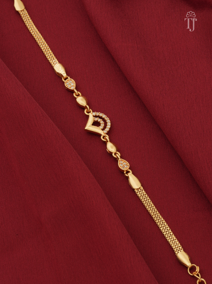 A gold chain bracelet with a central crescent moon and diamond motif, displayed diagonally on a deep red fabric background.