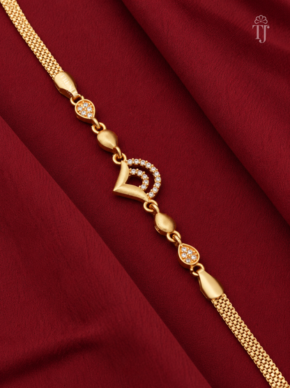 A gold chain bracelet with a central crescent moon and heart motif embellished with small clear stones, displayed diagonally on a draped dark red fabric background.