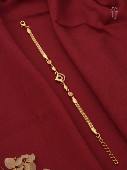 A gold-toned chain bracelet with a central heart-shaped motif and small circular details, laid diagonally on draped deep red fabric.