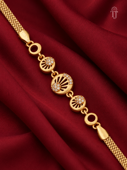 A gold chain bracelet with three circular fan-shaped charms, two of which are adorned with small clear stones, displayed on a draped dark red satin fabric. A small 'TJ' logo is visible in the top right corner.