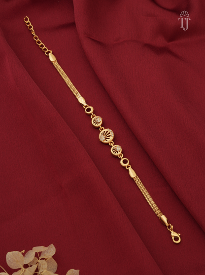 A gold-toned chain bracelet with decorative oval and sunburst motifs, laid diagonally on draped deep red fabric.