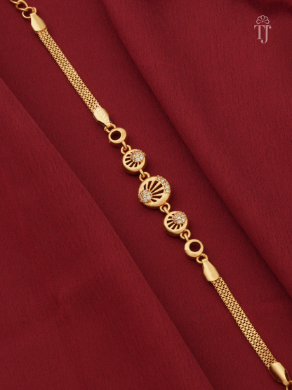 A gold chain bracelet with three circular decorative charms, two of which feature small clear stones, displayed diagonally on a draped dark red fabric background.