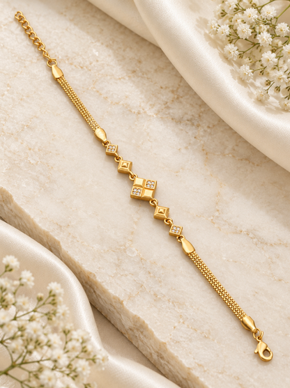 A gold chain bracelet with small diamond-shaped links, some set with clear stones, displayed on a light beige stone slab with white fabric and baby's breath flowers.