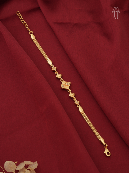 A gold-toned chain bracelet with small diamond-shaped motifs and a central square charm, displayed diagonally on draped dark red fabric.