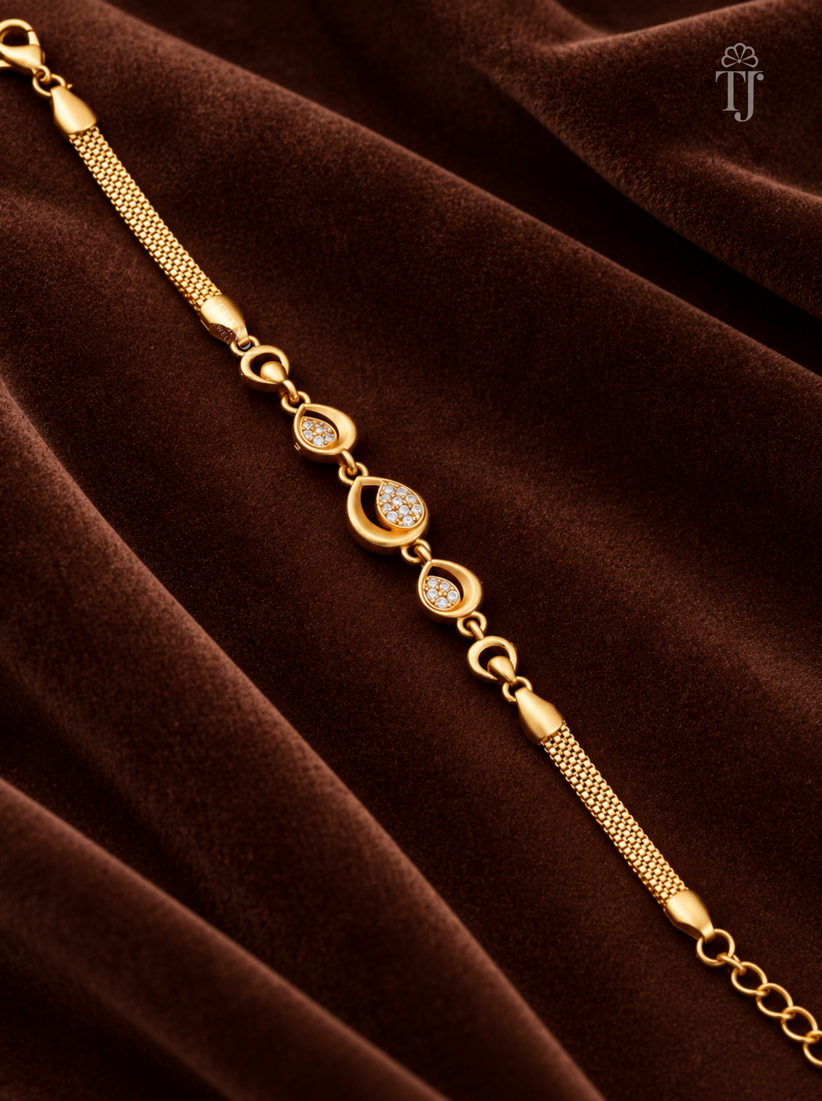 A gold-toned chain bracelet with teardrop-shaped settings set with small clear stones, displayed diagonally on a draped dark brown velvet fabric background.