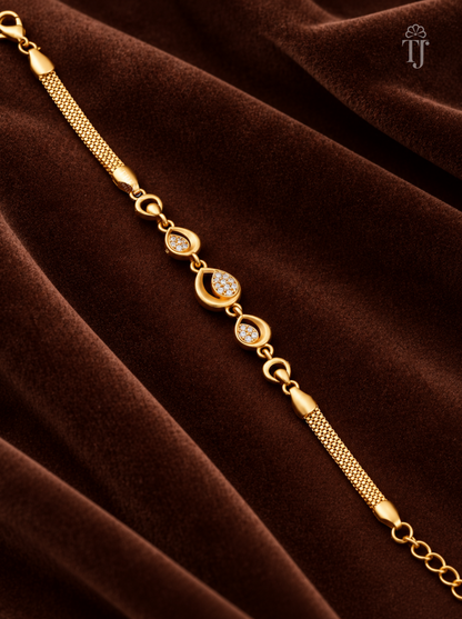 A gold-toned chain bracelet with teardrop-shaped settings set with small clear stones, displayed diagonally on a draped dark brown velvet fabric background.