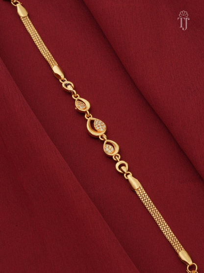 A gold chain bracelet with decorative oval links, some featuring small clear stones, displayed diagonally on a draped dark red fabric background.