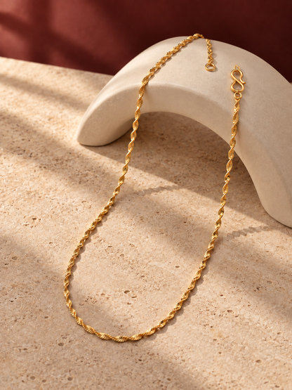 Twisted gold plated chain draped over cream stone arch in soft sunlight